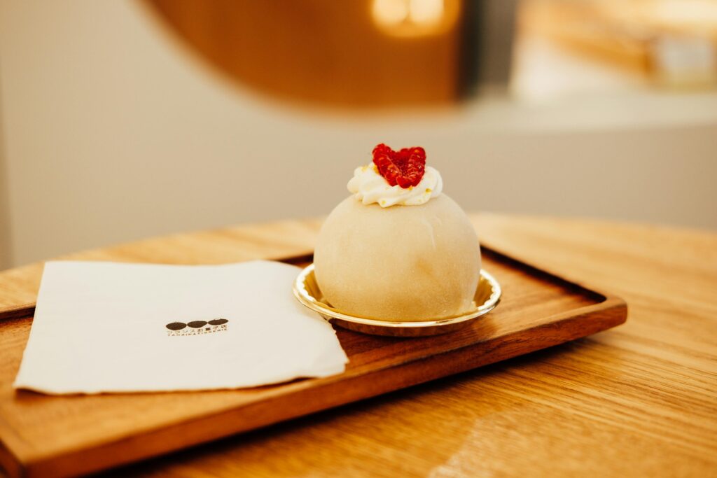 Delicious mochi dessert topped with raspberry served on a wooden tray in a café setting.