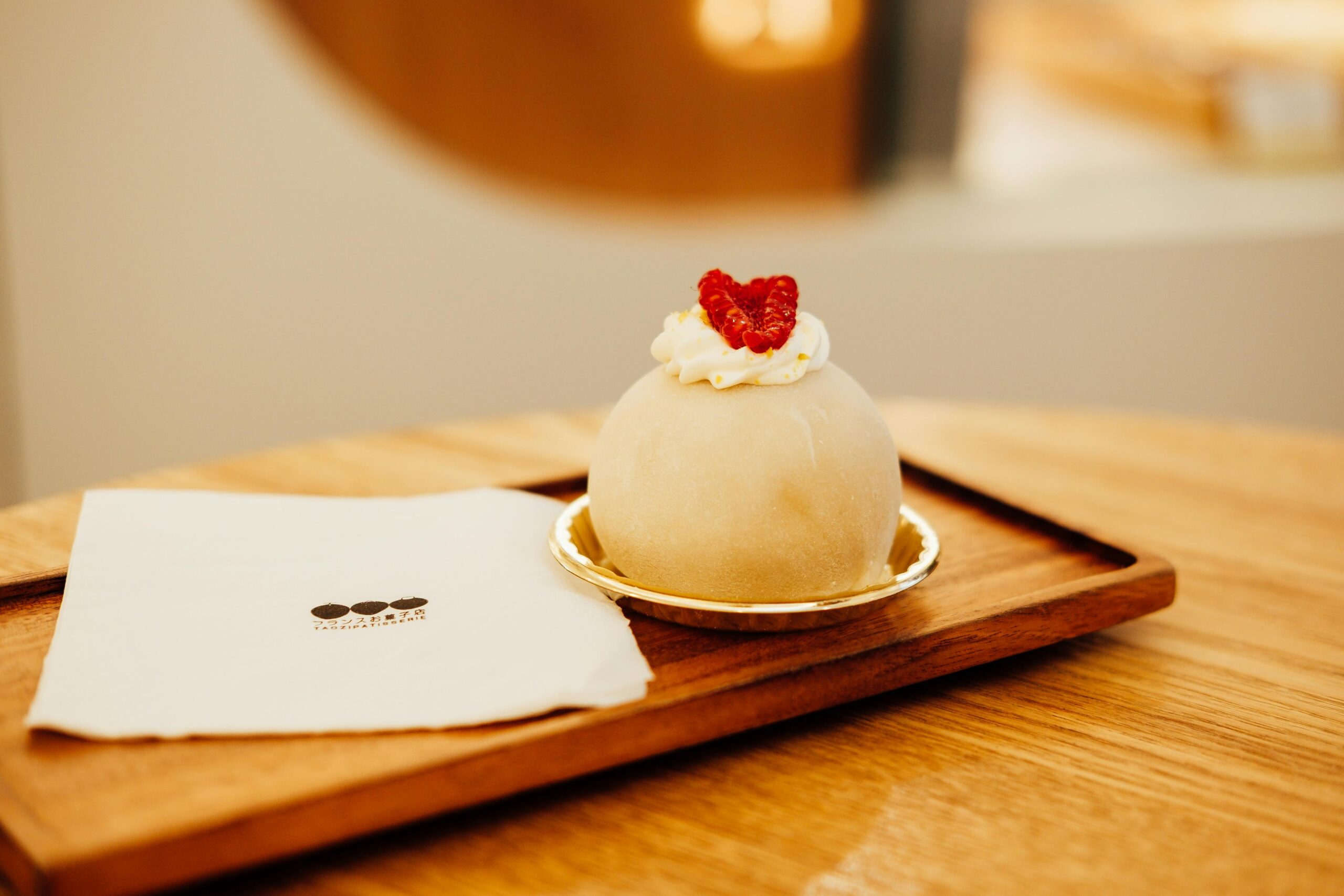 Delicious mochi dessert topped with raspberry served on a wooden tray in a café setting.